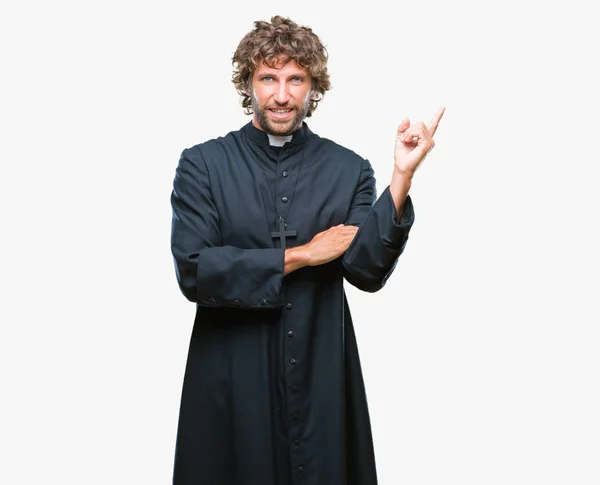 英俊的西班牙天主教牧师男子在孤立的背景与一个很大的微笑在脸上 用手和手指指着一边看着镜头 — 图库照片