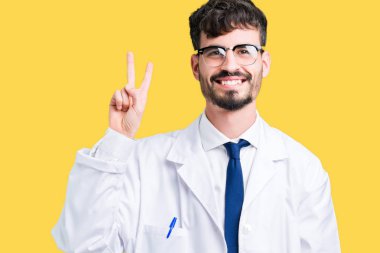 Gösterilen ve parmakları ile işaret izole arka plan üzerinde beyaz önlük giyen genç profesyonel bilim adam ikincisi ise kendinden emin ve mutlu gülümseyerek.