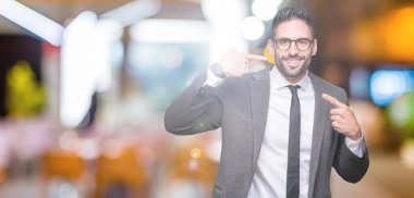 Genç yakışıklı iş adamı kendine güvenen gösterilen ve işaret parmakları diş ve ağız ile gülümseyen izole arka plan üzerinde. Sağlık kavramı.