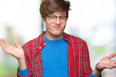 Üzerinde gözlük takan genç yakışıklı öğrenci adam arka plan clueless ve şaşkın bir ifadeyle kollar ve eller kaldırdı izole. Şüphe kavramı.