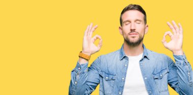 Yakışıklı adam mavi gözleri ve denim ceket giyen sakal rahatla ve gülümseyen gözlerle parmak ile meditasyon jest yapıyor kapalı. Yoga kavramı.