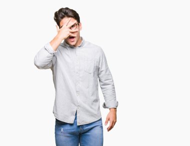 Mahcup ifadeyle parmaklarımın arasından seyir yüz ve gözler el ile kapsayan şok bakmak izole arka plan üzerinde gözlük takan genç yakışıklı adam.