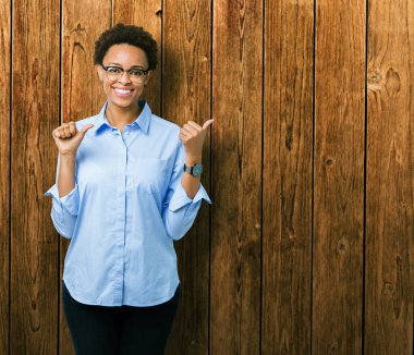 Genç güzel Afro-Amerikan iş kadını izole arka plan üzerinde emin gülümseyen arkasından el ve kadar başparmak ile işaret