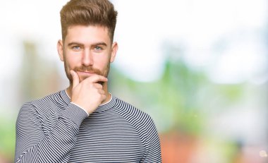 Emin çapraz kollar ve çeneme kaldırdı el ile gülümseme ile kameraya bakarak çizgili Süveter giyen genç yakışıklı adam. Pozitif düşünce.