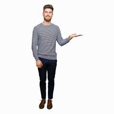 Neşeli sunulması ve kameraya bakarak avucunun ile işaret gülümseyen çizgili süveter giyen genç yakışıklı adam.