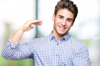 Genç yakışıklı iş adamı izole arka plan eller eller büyük gösterilen ve büyük boy işareti, ölçü birimi sembolü ile üzerinden. Kameraya bakarak gülümsüyordu. Ölçüm kavramı.