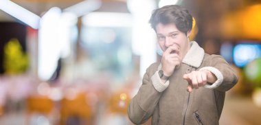 Genç yakışıklı adam giyen kış ceket izole üzerinde arka plan sizin parmak el kamerasıyla ağzına, utanç ifadesi işaret eden gülme