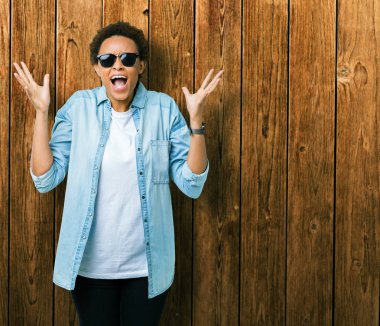 Güzel genç Afro-Amerikan kadın üzerinde güneş gözlüğü takıyor deli kutluyor arka plan izole ve silah ile başarı için yükseltilmiş ve açık gözleri heyecanlı çığlık hayrete düşürdü. Kazanan kavramı