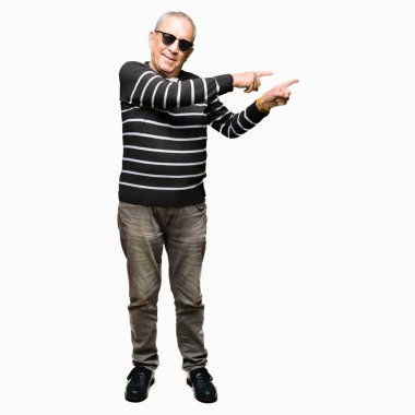 Yakışıklı kıdemli adam giyen kış kazak ve gülümseyen ve iki elleri ve parmakları ile tarafına işaret kamera bakarak güneş gözlüğü.