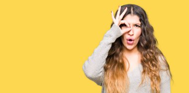 Sürpriz yüz, göz parmaklarının arasından seyir ile ok jest yapıyor Kış elbise giyen genç güzel kadın şok. İmansız ifade.