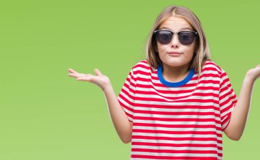Genç güzel kız izole arka plan clueless ve şaşkın bir ifadeyle kollar ve eller kaldırdı üzerinde güneş gözlüğü takıyor. Şüphe kavramı.