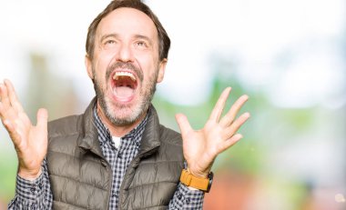 Orta yaş yakışıklı adam giyen kış yelek kutluyor deli ve çığlık kaldırdı ve açık gözleri hayret silah ile başarı için heyecanlı. Kazanan kavramı