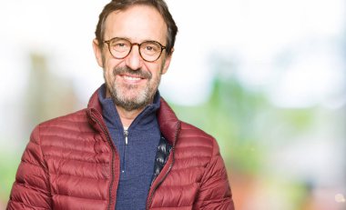 El ele tutusun ve rahat ve neşeli gülümseyen parmak çarpı işareti orta yaş yakışıklı adam gözlük ve kış ceket. Başarı ve iyimser