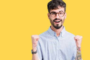 Yakışıklı delikanlı izole arka plan üzerinde kutluyor gözlük takan şaşırttı ve başarı için kaldırdı kollarını açarak hayret ve gözleri açık. Kazanan kavramı.