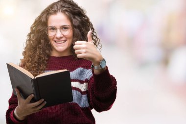 Genç esmer kız ok işareti, başparmak ile parmak, mükemmel işareti yapıyor kocaman bir gülümseme ile izole arka plan üzerinde mutlu gözlük takan bir kitap okuma