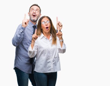 Orta yaş İspanyol çift izole arka plan üzerinde gözlük aşık hayret ve yukarıya bakıyor ve parmakları ile işaret ve silah kaldırdı şaşırttı.