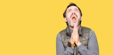 Orta yaş yakışıklı adam yalvarıyor ve umut ifade yüzünde çok duygusal ve endişe ile birlikte elleriyle dua kış yelek giyiyor. Bağışlanmak. Din kavramı.