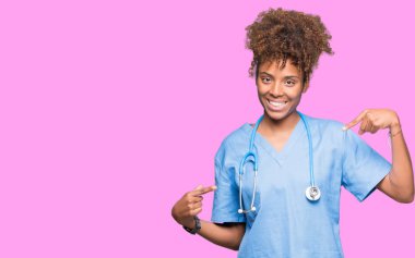 Yüzünde gülümseme ile kendinden emin görünüyorsun, kendini gururlu ve mutlu parmakları ile işaret izole arka plan genç Afro-Amerikan doktor kadın.