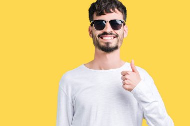 Genç yakışıklı adam hareketi el ile mutlu yaşasın yapıyor izole arka plan üzerinde güneş gözlüğü takıyor. Kameraya bakarak başarı gösteren ile ifade onaylama.