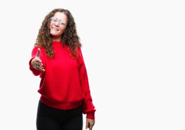 Güzel esmer kıvırcık saçlı Genç kız dostu sunan el sıkışma tebrik ve davet edici olarak gülümseyen izole arka plan üzerinde gözlük ve kış kazak giyiyor. Başarılı iş.