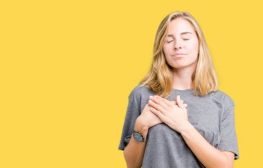 Güzel genç kadın üzerinde gülümseyen izole arka plan ile büyük boy rahat t-shirt giyen kapalı gözler ve yüzünde minnettar jest ile göğüs üzerinde eller. Sağlık kavramı.