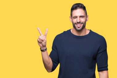 Mutlu yüz zafer işareti yaparken kameraya göz kırpıyor ile gülümseyen izole arka plan üzerinde kazak giyen genç yakışıklı adam. İki numaralı.