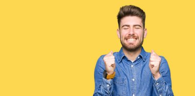 Genç yakışıklı sarışın adam rahat kot gömlek kolları olan başarı için heyecanlı zafer kutluyor gülümseyen kaldırdı. Kazanan kavramı.