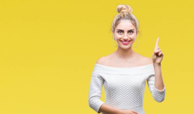 Genç güzel sarışın ve mavi gözlü kadın ve parmak gülümseyen süre bir numara ile kendinden emin ve mutlu yukarıyı gösteren izole arka plan.