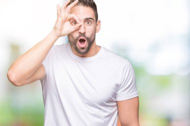 Sürpriz yüz, göz parmaklarının arasından seyir ile ok jest yapıyor izole arka plan üzerinde rahat beyaz t-shirt giyen genç adam şok. İmansız ifade.