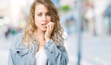 Stresli ve gergin ile izole arka plan üzerinde kot ceket giyen güzel genç sarışın kadın tırnak ısırma dudaklarından eller. Anksiyete sorunu.