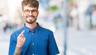 Beckoning gel burada mutlu ve gülümseyerek el davet ile jest arka plan üzerinde gözlük takan genç yakışıklı adam izole