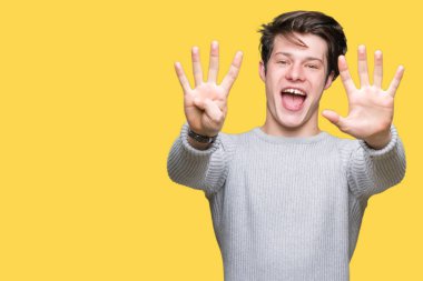 Gösterilen arka plan üzerinde kış kazak giyen genç yakışıklı adam izole ve parmakları ile işaret numara 9 kendinden emin ve mutlu gülümseyerek süre.