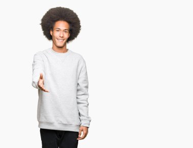 Afrikalı-Amerikalı genç afro saçlı tebrik ve konuksever dost sunan karşılıklı gülümseyen sportif kazak giyiyor. Başarılı iş.