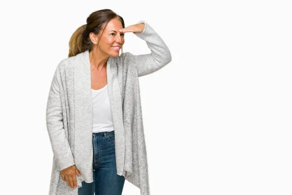 美丽的中年成年妇女穿着冬季毛衣在孤立的背景非常高兴和微笑看远与手超过头 搜索概念 — 图库照片