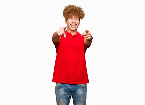 アフロの髪を指でカメラに赤 シャツ ポインティング 肯定的な陽気な笑顔を身に着けている若いハンサムな男 — ストック写真