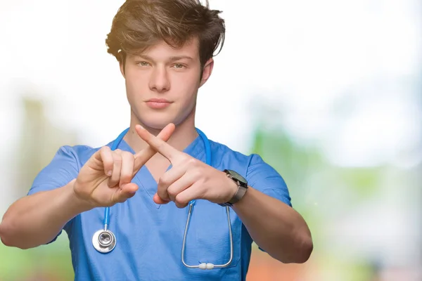 年轻的医生穿着医疗制服在孤立的背景拒绝表达交叉手指做负号 — 图库照片