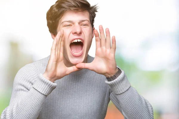 Young handsome man wearing winter sweater over isolated background Shouting angry out loud with hands over mouth