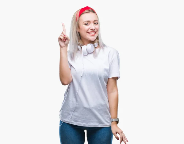 年轻的金发碧眼的女人戴着耳机听音乐在孤立的背景手指与成功的想法 离开和快乐 — 图库照片