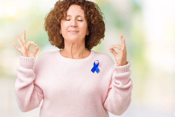 Middle ager senior woman wearing changeable blue color ribbon awareness over isolated background relax and smiling with eyes closed doing meditation gesture with fingers. Yoga concept.
