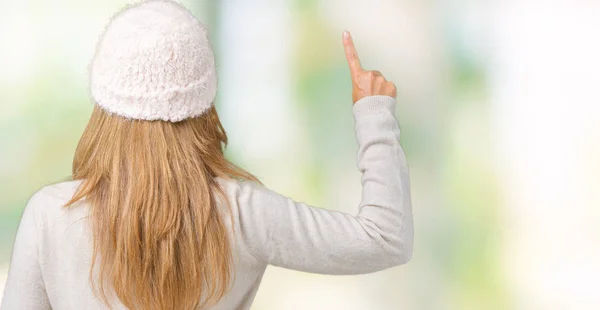 Beautiful middle age woman wearing winter sweater and hat over isolated background Posing backwards pointing behind with finger hand