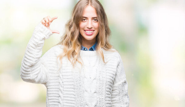 Beautiful young blonde woman wearing winter sweater over isolated background smiling and confident gesturing with hand doing size sign with fingers while looking and the camera. Measure concept.