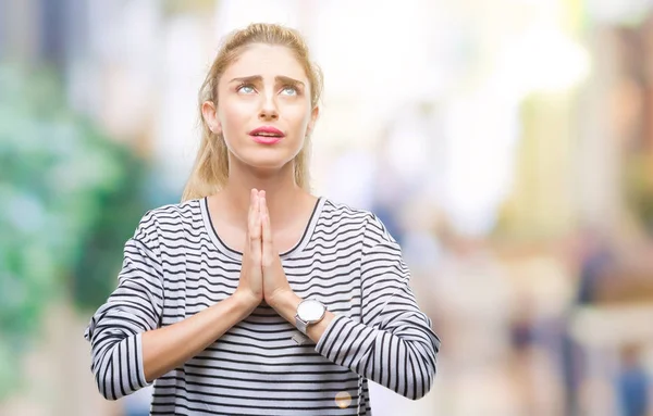 Young beautiful blonde woman wearing stripes sweater over isolated background begging and praying with hands together with hope expression on face very emotional and worried. Asking for forgiveness. Religion concept.