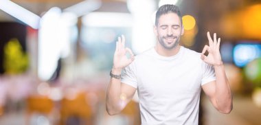 Casual beyaz t-shirt izole arka plan üzerine dinlenmek giydiği ve gözleri ile gülümseyen genç adam parmak ile meditasyon jest yapıyor kapalı. Yoga kavramı.