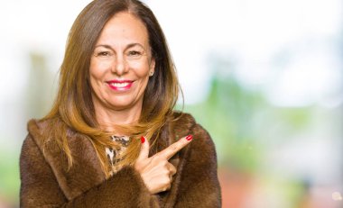 Neşeli bir gülümseme ile el ve parmak kadar yan yüzünde mutlu ve doğal ifade ile işaret yüz vizon kürk giyen güzel orta yaş zarif kadın