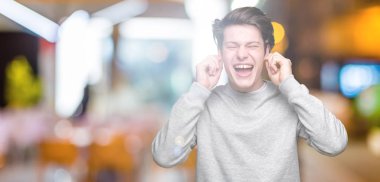 Yüksek sesle müzik gürültü rahatsız ifade parmaklarıyla kulaklarıyla kapsayan izole arka plan üzerinde sweatshirt giyen genç yakışıklı sportif adam. Sağır kavramı.