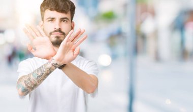 İzole arka plan ret ifade geçiş silah ve avuç içi eksi işareti, kızgın surat yapıyor üzerinde beyaz t-shirt giyen genç yakışıklı adam