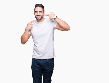 Kendinden emin gösterilen ve işaret parmakları diş ve ağız ile gülümseyen izole arka plan üzerinde rahat beyaz t-shirt giyen genç adam. Sağlık kavramı.