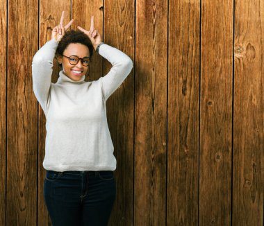 Neşeli gülümseyen izole arka plan tavşan kulakları, komik ve çılgın baş parmaklar ile poz üzerinde gözlük takan genç güzel Afrikalı-Amerikalı kadın