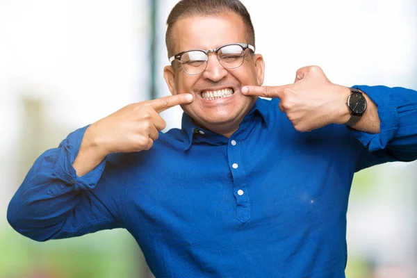 中年阿拉伯男子戴眼镜在孤立的背景微笑自信显示和指向用手指的牙齿和嘴 健康理念 — 图库照片