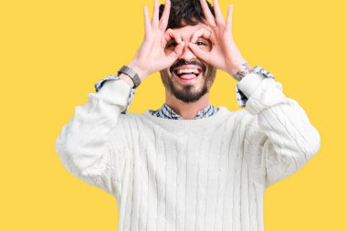 Dilini, parmaklarının arasından baktığını yapışmasını dürbün gibi ok jest yapıyor izole arka plan üzerinde kış kazak giyen genç yakışıklı adam. Deli ifade.